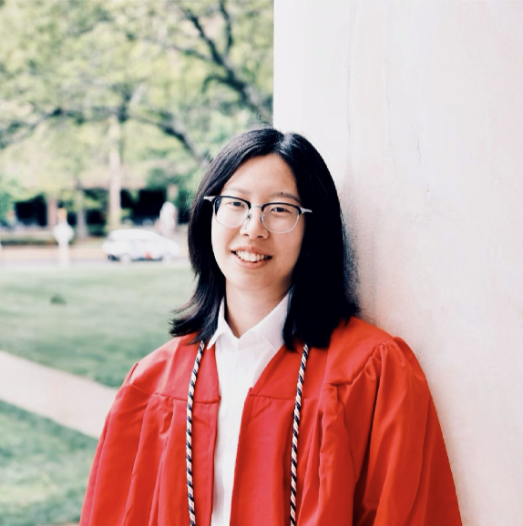 Student wearing red graduation attire with grass and trees in the background